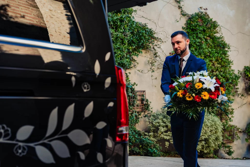 Agent funéraire transportant une composition florale pour une cérémonie d'obsèques.