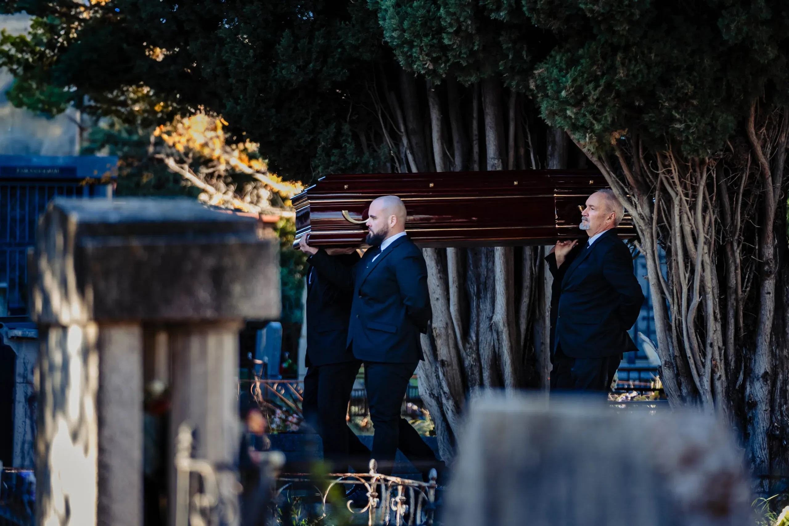 Porteurs de pompes funèbres transportant un cercueil dans un cimetière.