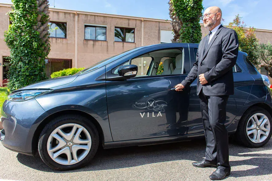Conseiller en costume à côté d'un véhicule des pompes funèbres Vila.